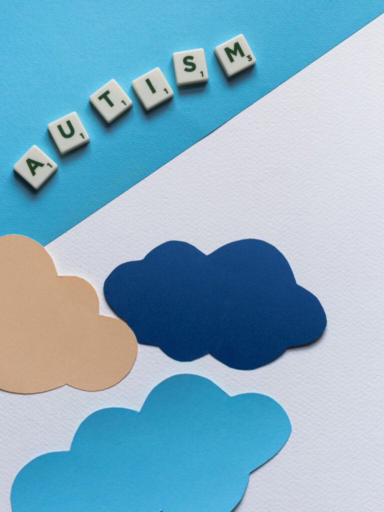 A conceptual flat lay featuring clouds and the word 'autism' spelled with tiles.